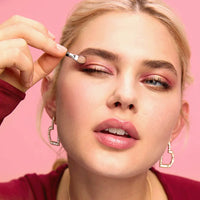 Woman applying makeup with a brush against a pink background