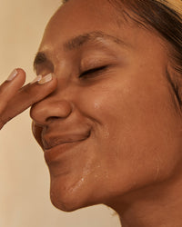 Close-up of a person's face with a hand touching their cheek against a beige background