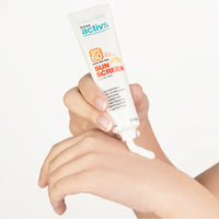 Hand applying sunscreen cream from a tube labeled 'Super Activs' on a white background
